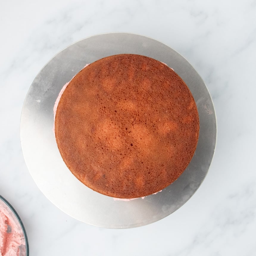 Two stacked cake layers with frosting between them on a metal turntable.