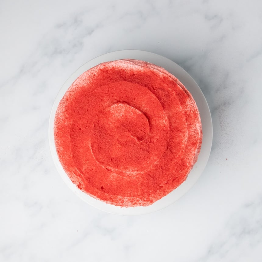 Frosted gluten free strawberry cake topped with a layer of bright red powder.