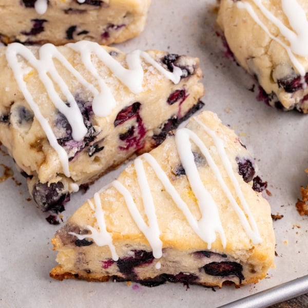 A close-up of a few baked blueberry scones with melted sugar crystals and a white glaze drizzle.