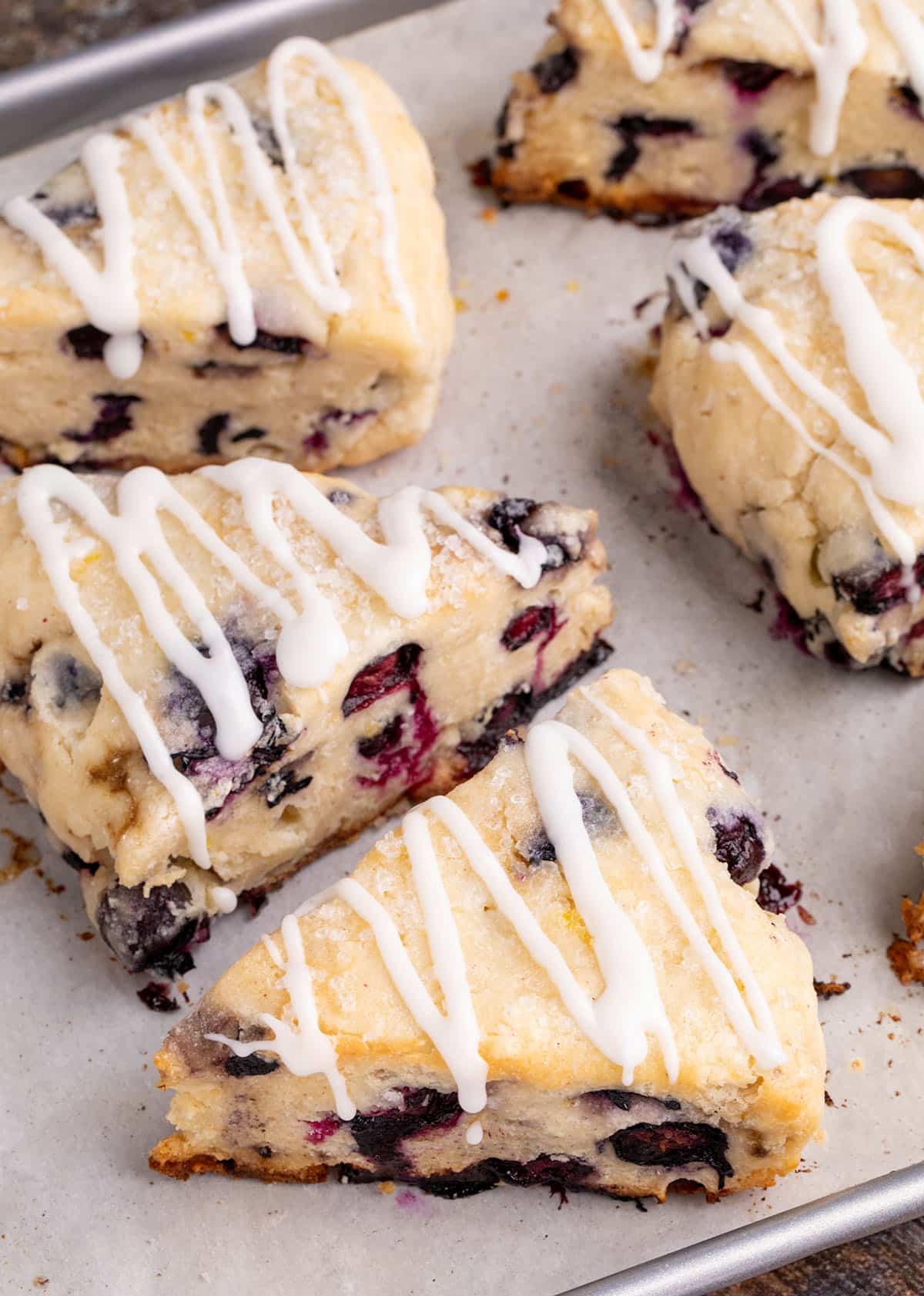A group of baked scones with a white glaze drizzle and sparkling sugar on a baking sheet.