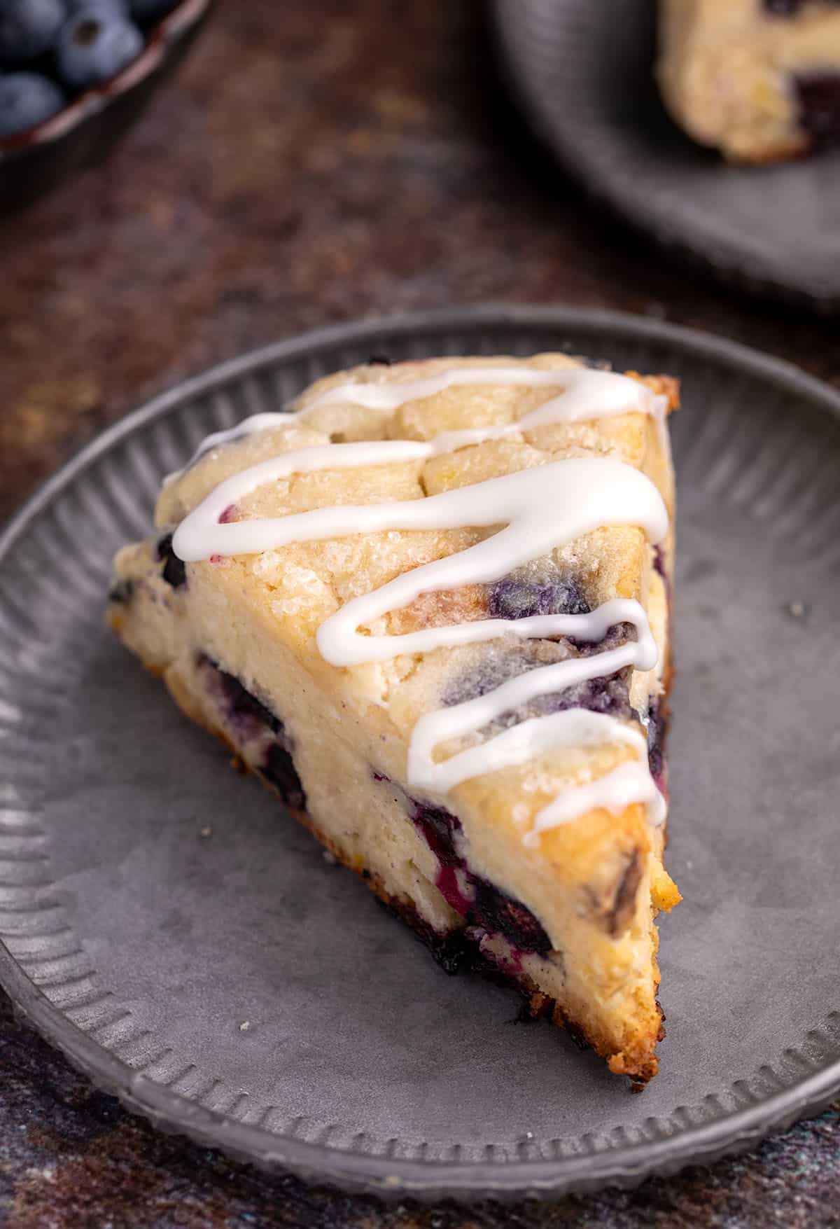 A single baked scone, cut into a wedge, on a small, dark pewter plate.