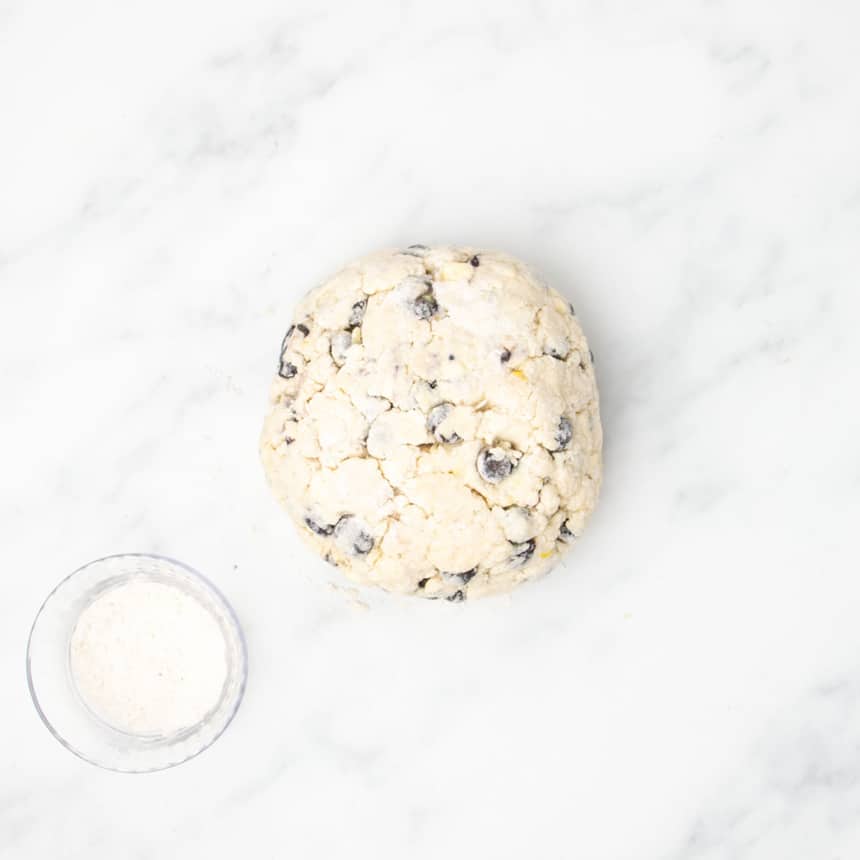 The dough shaped into a round disc on a marble surface next to a small glass bowl of extra gluten free flour.