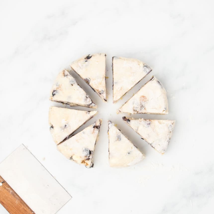 The dough round cut into eight triangular wedges, arranged in a circle on a marble surface.