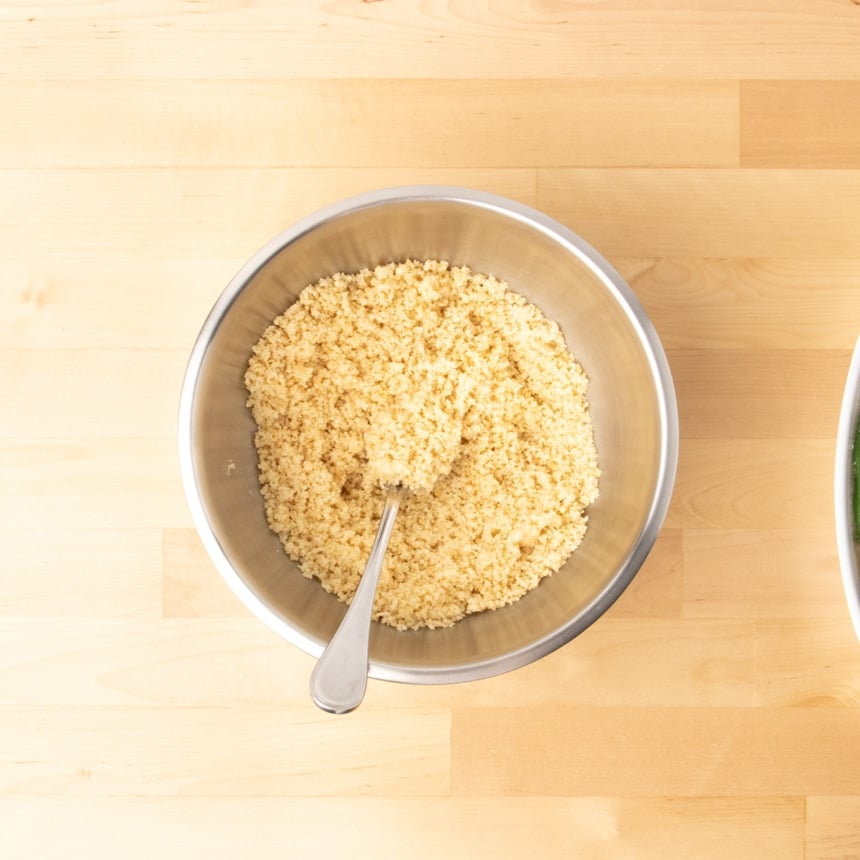 small round metal mixing bowl with tan coarse bread crumbs mixed with melted butter with a metal mixing spoon in the center