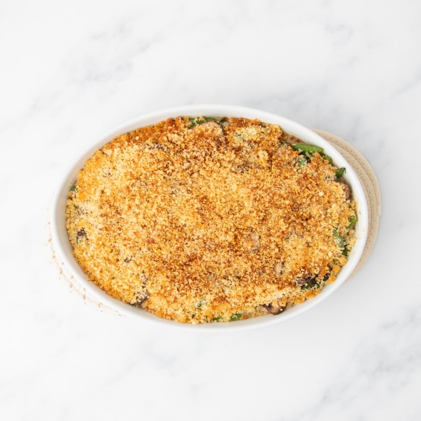 same casserole dish now with a golden brown topping after being baked in the oven, on cloth trivets to protect the marble countertop below