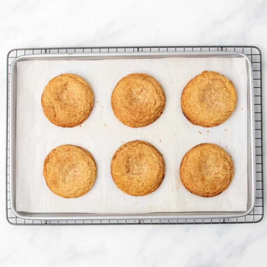 same baking sheet, now with 6 baked brown round gluten free snickerdoodle cookies, cooling on wire rack