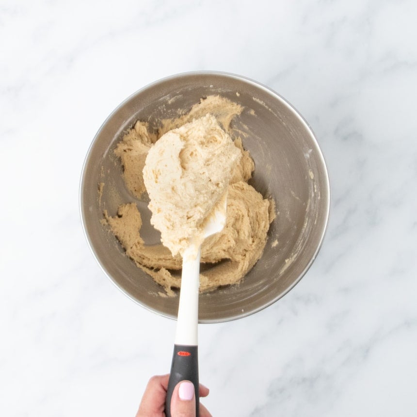 beaten very pale brown raw snickerdoodle cookie dough partly on white spatula and partly in metal mixing bowl