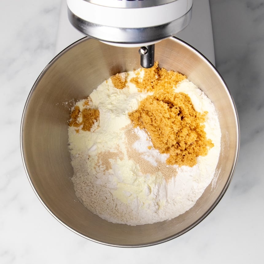 round metal mixing bowl in white stand mixer with yellow, white, tan and light brown dry ingredient powders, unmixed