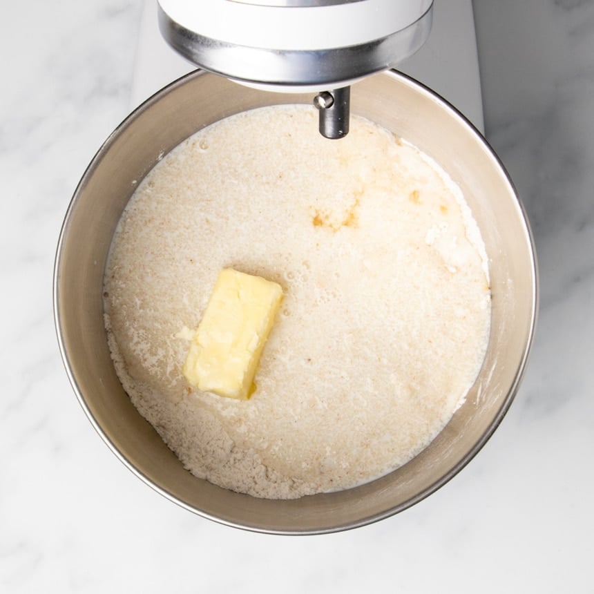 cloudy milk mixture adding on top of dry ingredients in bowl, with softened stick of butter on top