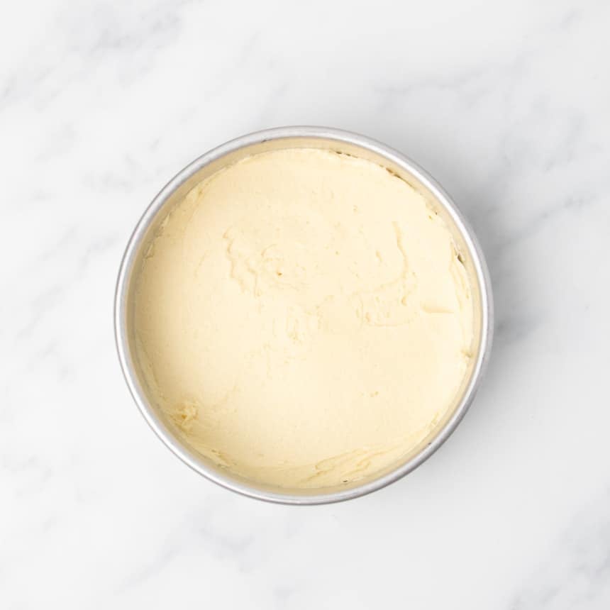 Plain yellow raw cake batter spread evenly on bottom of a round metal cake pan.