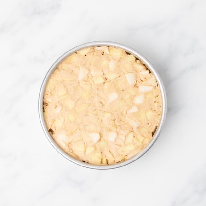 Unbaked cake batter with visible apple pieces spread in a round pan.