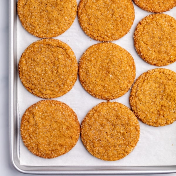 Closeup image of medium brown, round cookies with coarse sugar on top arranged in rows on a parchment-lined baking sheet.