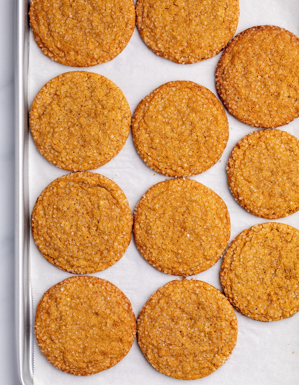 11 round, medium-brown colored cookies with sugar crystals on top cooling on a parchment-lined baking sheet.