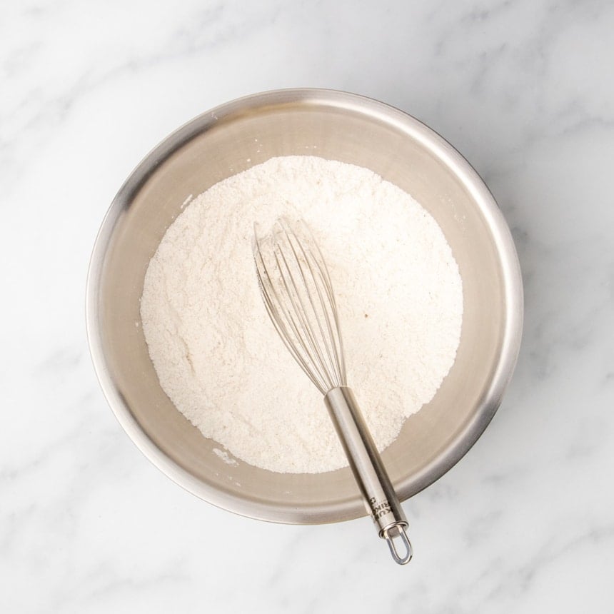 Dry ingredients whisked together in a stainless steel mixing bowl with a whisk.