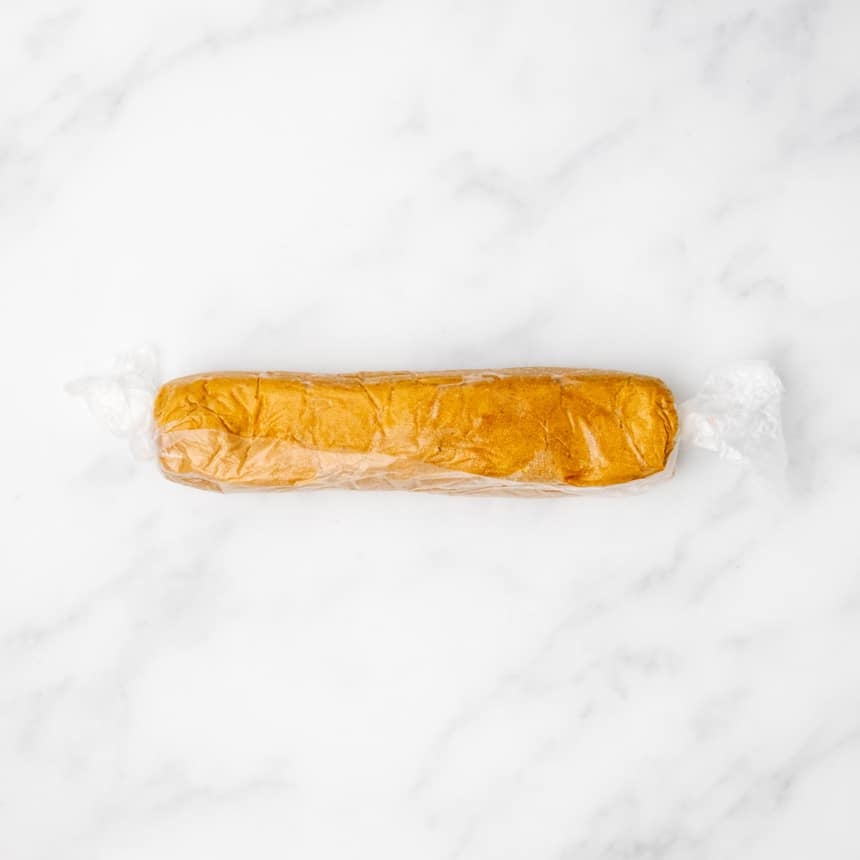 Brown raw cookie dough rolled into a log and wrapped in plastic wrap.