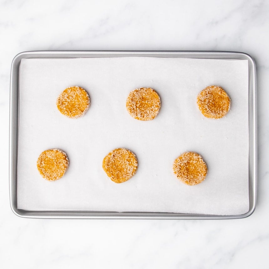Six sugar-coated cookie dough rounds spaced apart on a parchment-lined baking sheet.