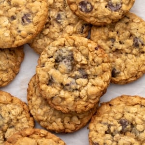 A close view of several golden brown oatmeal cookies with visible chocolate chips, overlapping each other on a white surface.