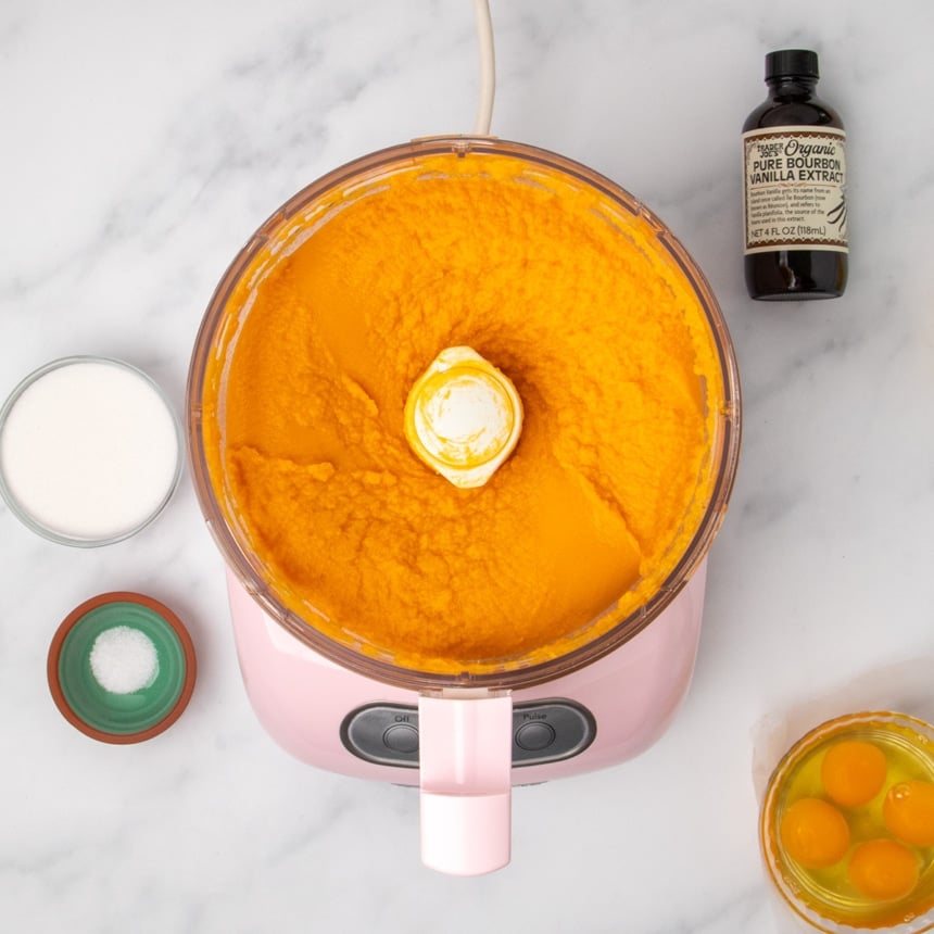 A food processor containing smooth pureed orange sweet potatoes surrounded by the same small bowls of other ingredients.