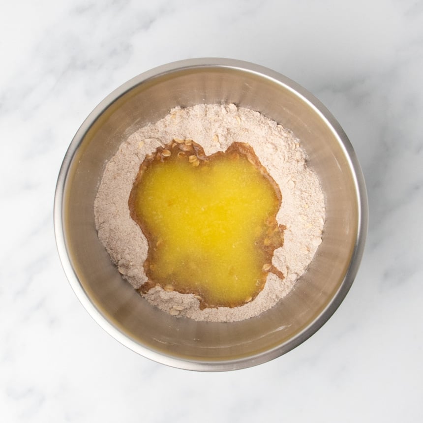 A metal mixing bowl holding dry ingredients with melted butter poured in the center, ready to be mixed.