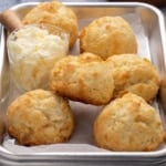 closeup of 6 small gluten free drop biscuits on a small metal tray with a glass container filled with whipped butter