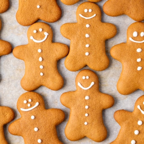 closeup overhead image of lots of brown man-shaped gluten free gingerbread cookies on white paper