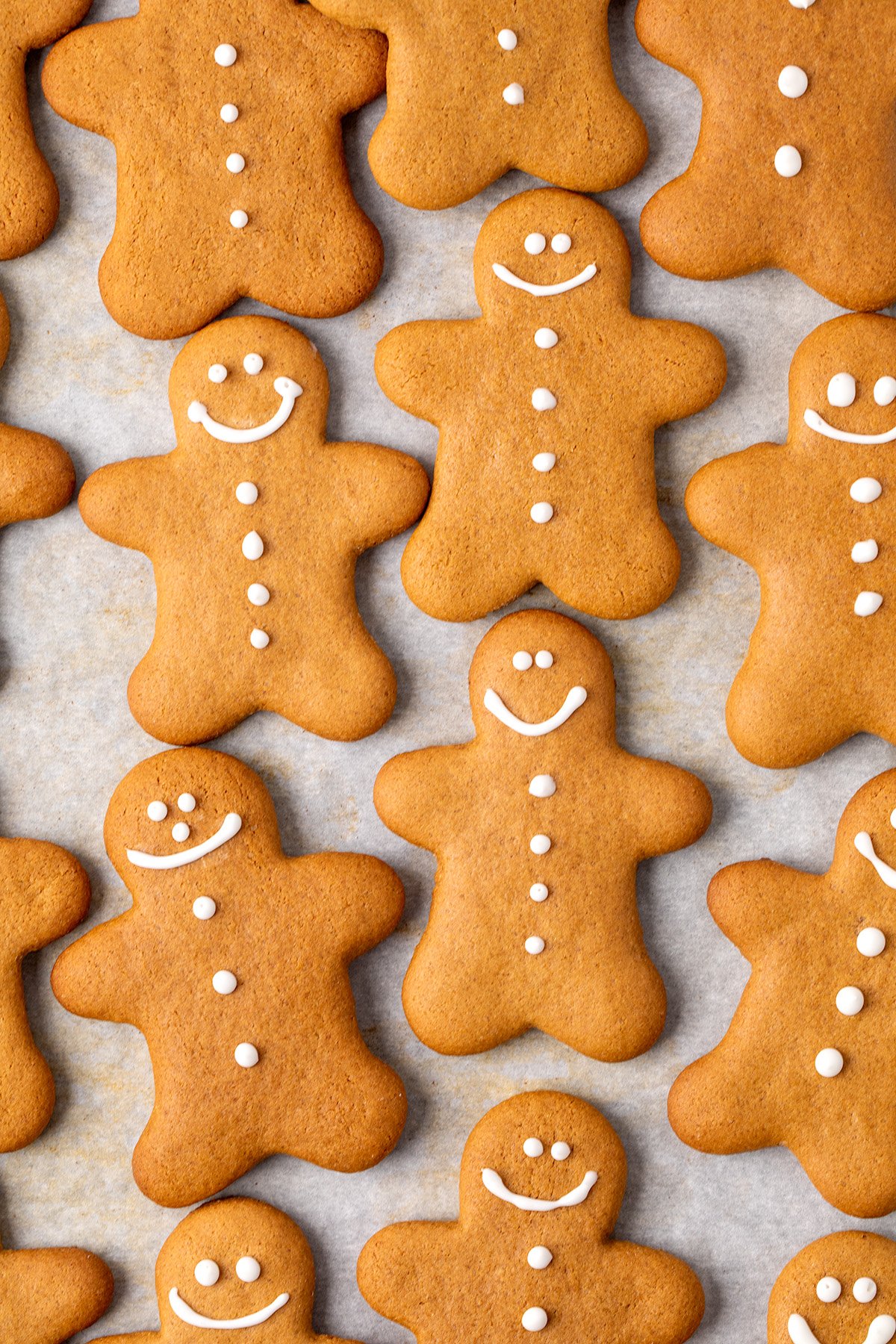 Multiple gingerbread men-shaped cookies arranged on white parchment paper, some decorated with simple white icing faces and buttons down the front