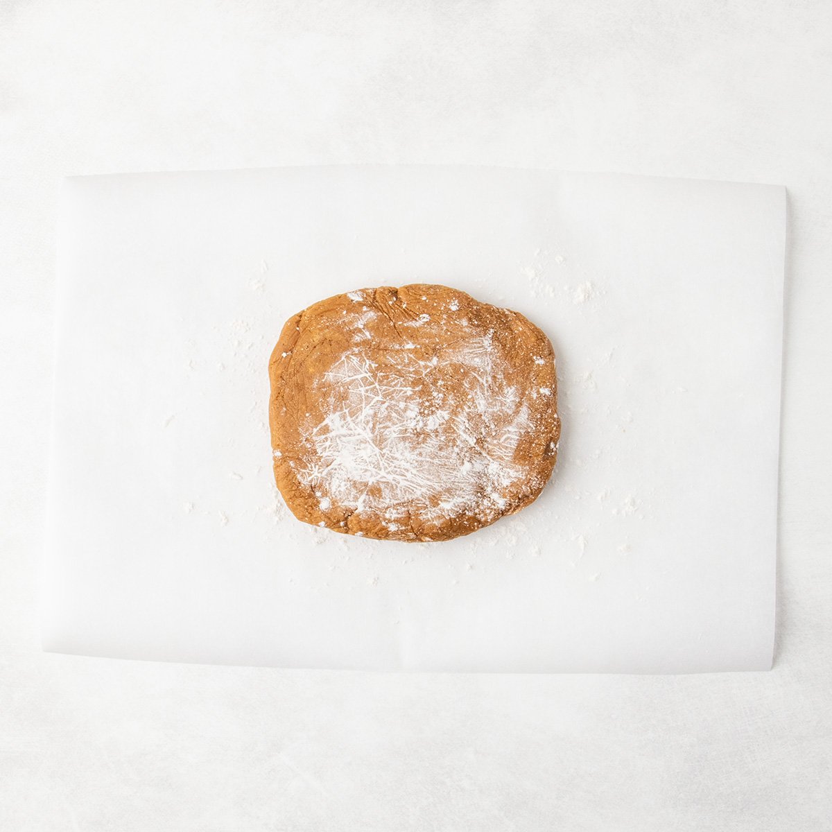 A flattened mound of raw brown cookie dough dusted with flour, placed on a sheet of parchment paper.