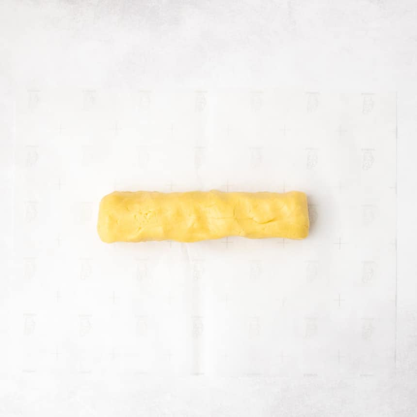 A long, even log of yellow dough resting on a sheet of parchment paper.