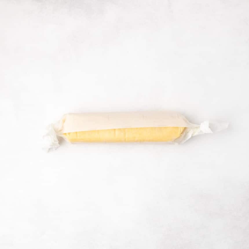 A log of yellow dough wrapped in parchment paper with the ends twisted closed.
