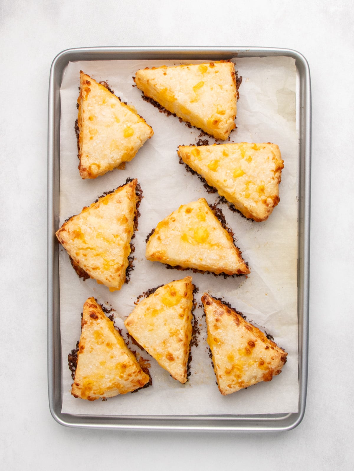 Baked triangular scones with browned edges sit on a parchment-lined baking sheet.