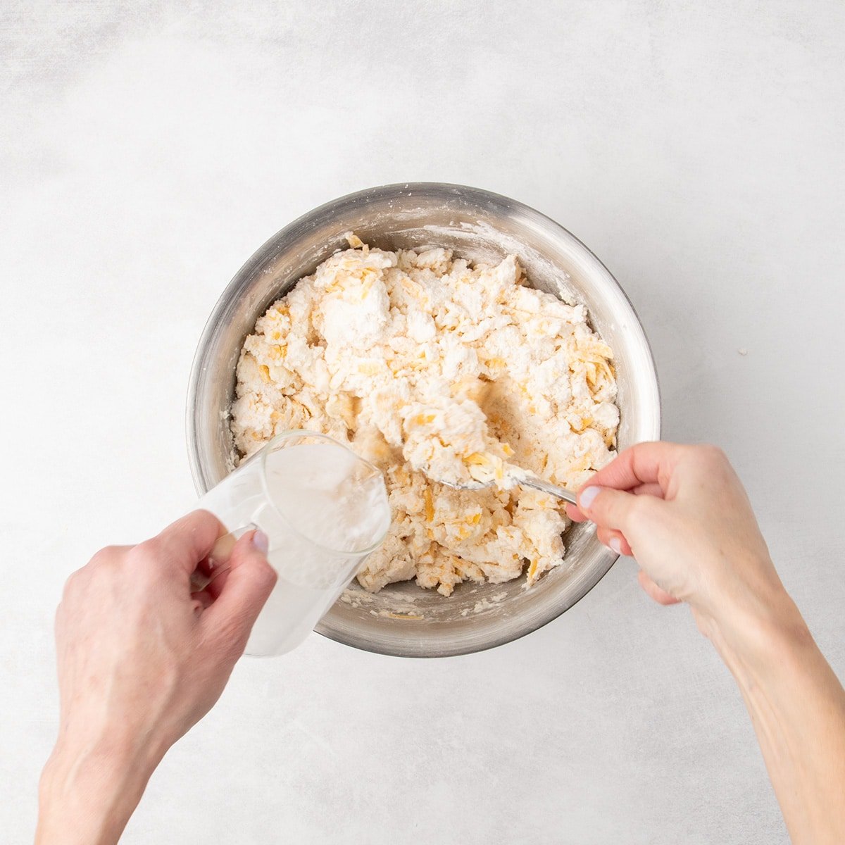 Cold water is poured into some dry spots in mixture in the same mixing bowl, with a spoon stirring inside.