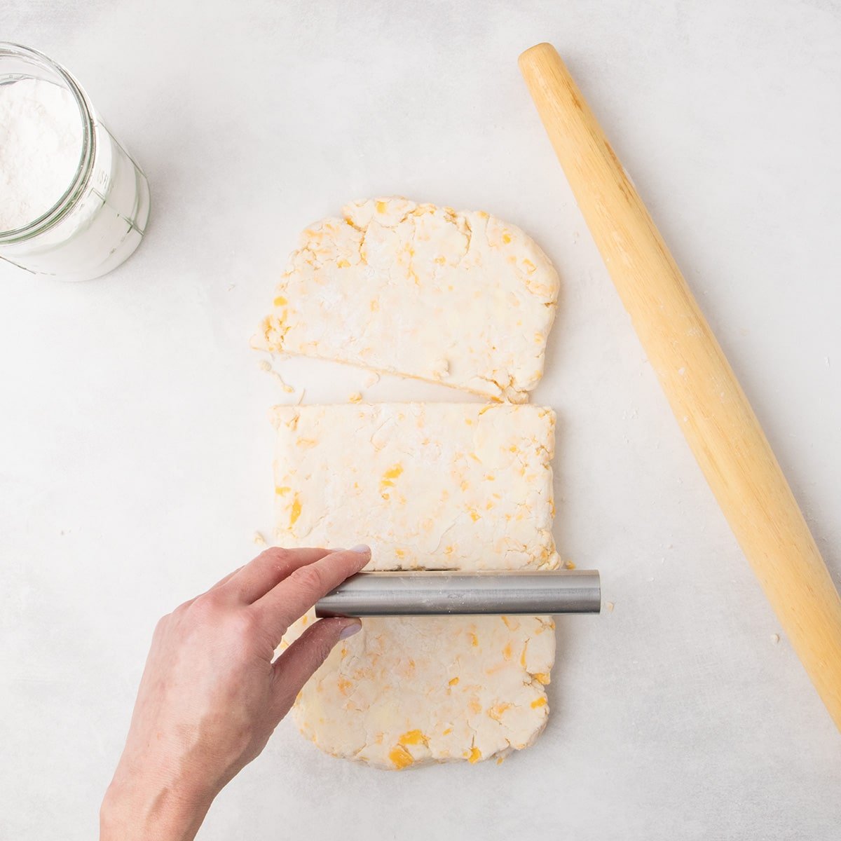The flattened dough has been cut in thirds across from one long side to another, with a metal bench scraper positioned above it.