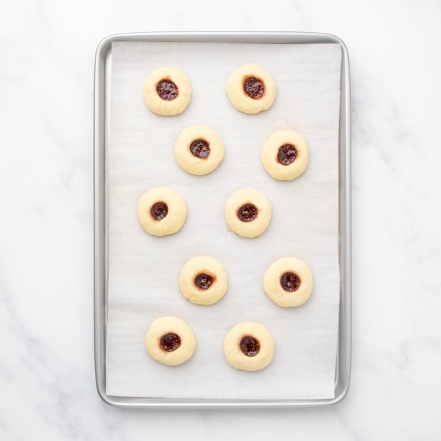 A baking sheet lined with parchment paper holding baked cookies with jam centers.