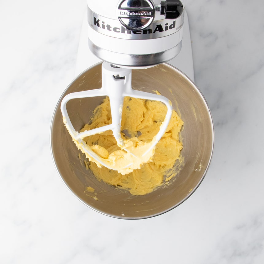Yellow batter mixture of egg yolk beaten into butter inside the same stand mixer bowl with the paddle attachment resting above it.