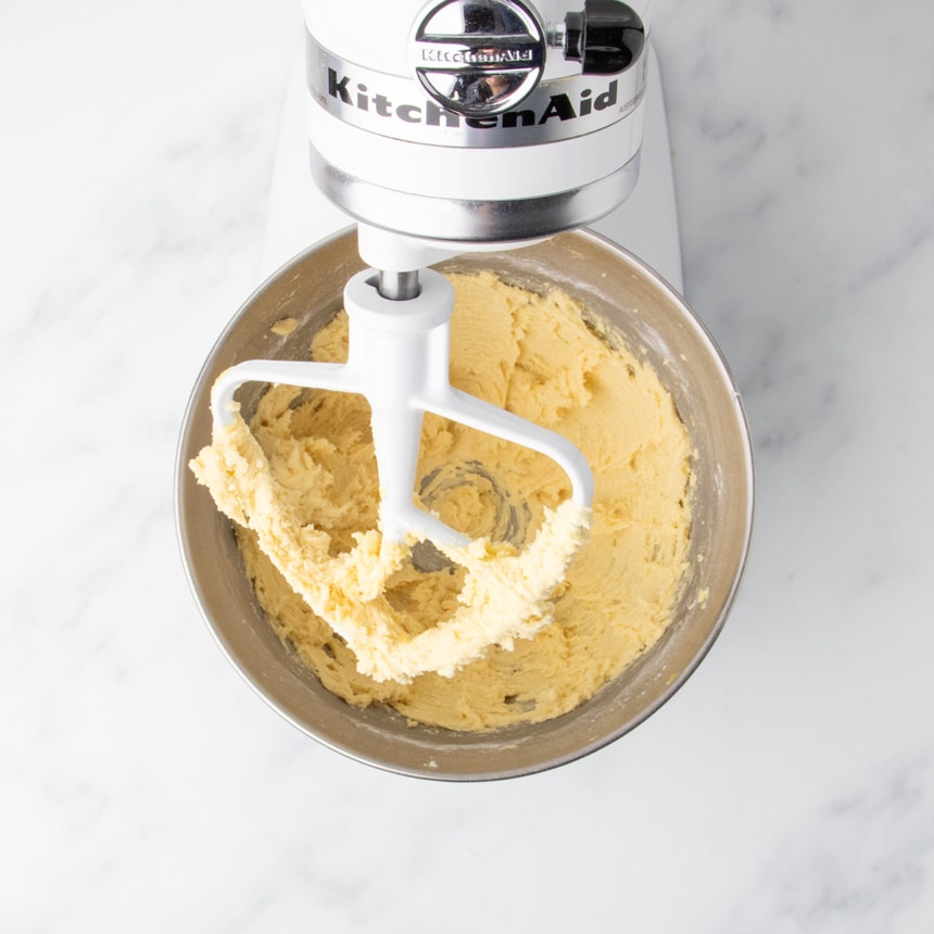 Cookie dough formed by adding flour to egg, butter and sugar mixture in a stand mixer bowl with some dough clinging to the paddle attachment.