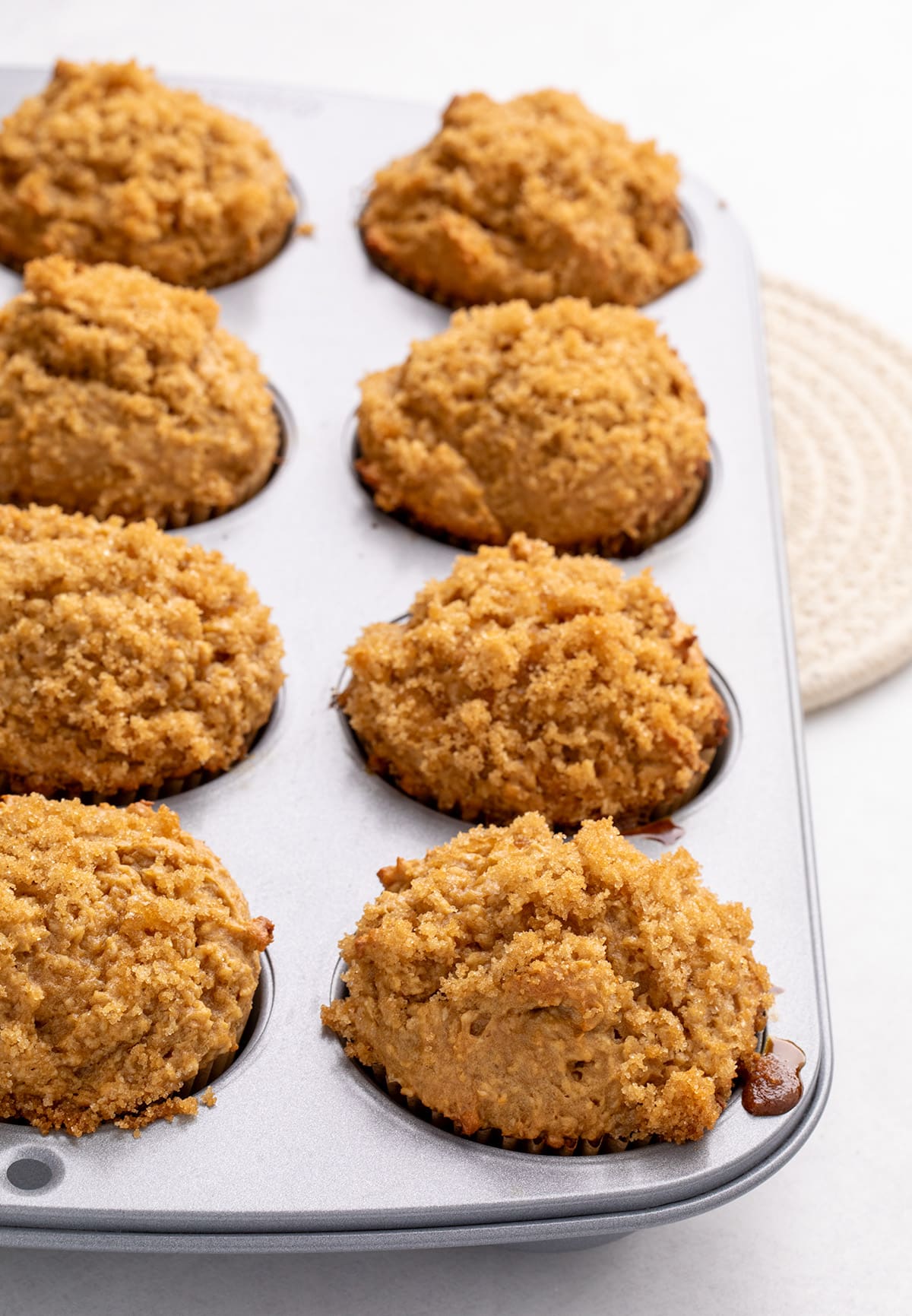 8 baked gluten free bran muffins in a metal muffin pan, each with a crumb-topped dome, viewed at an angle.