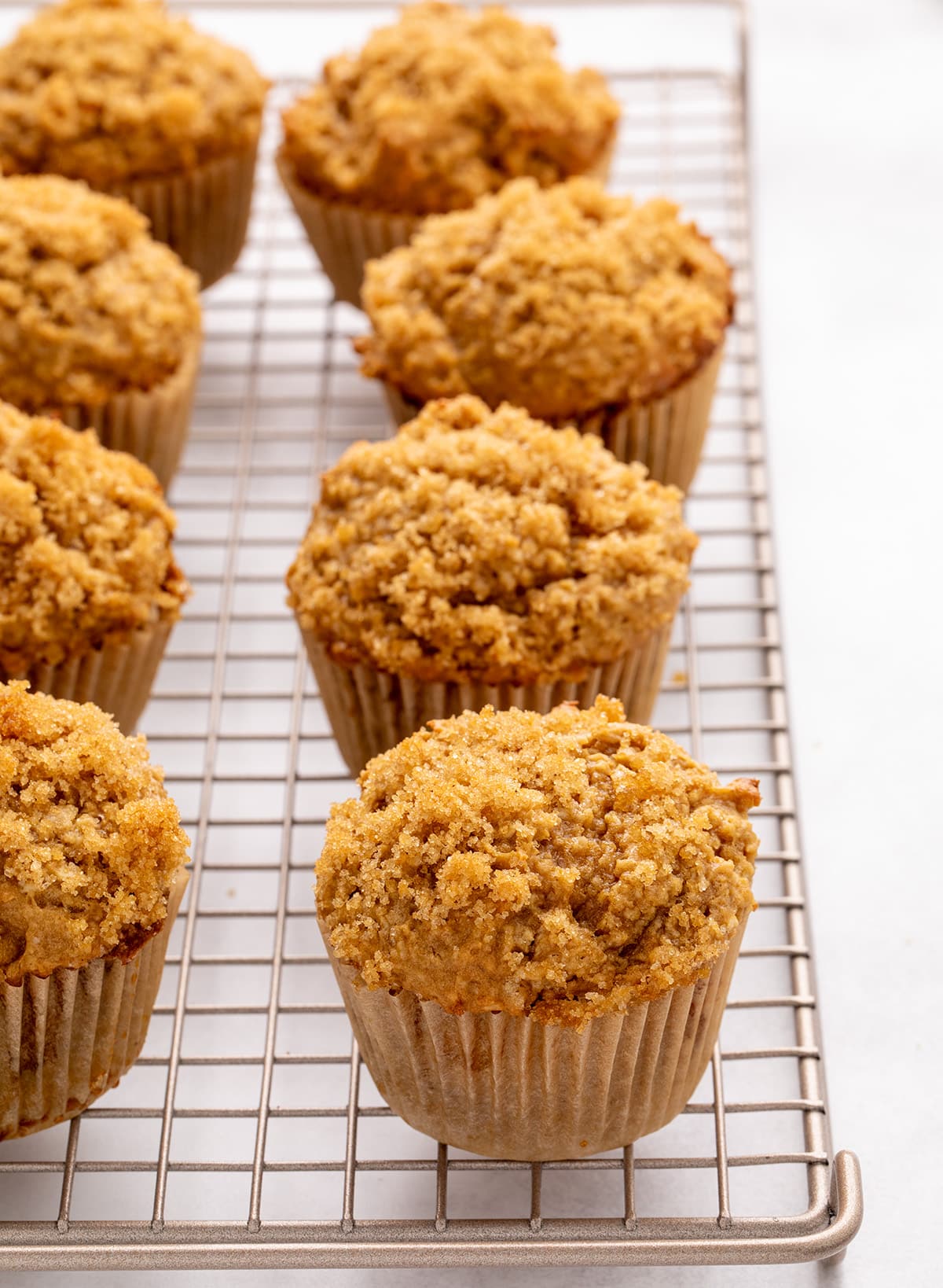 A row of baked muffins with crumbly brown sugar topping in paper liners on a wire cooling rack.