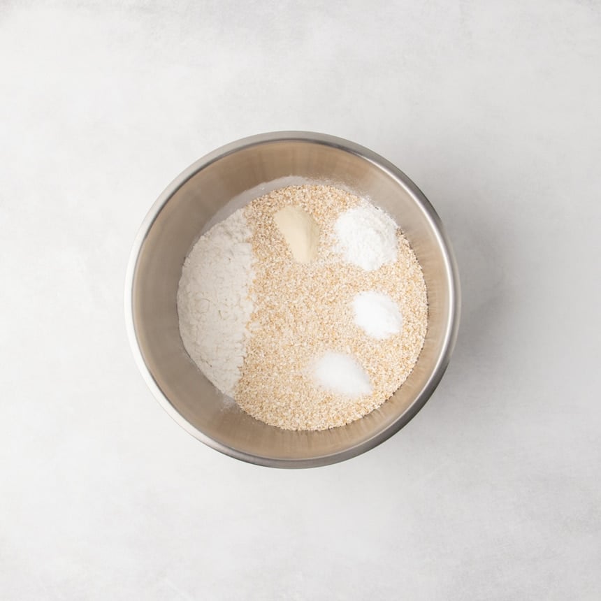 Dry ingredients in a stainless steel mixing bowl, with visible piles of white powders and coarse bran.