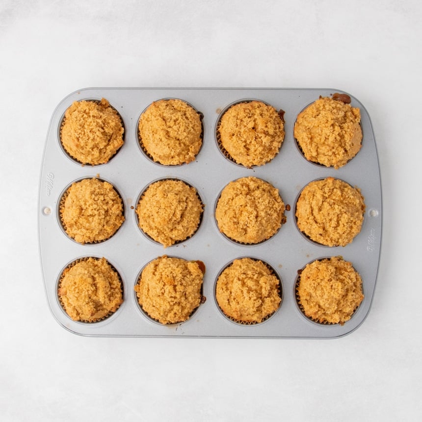 Baked muffins in a 12-cup muffin pan, with golden tops and texture of craggy brown sugar topping visible.