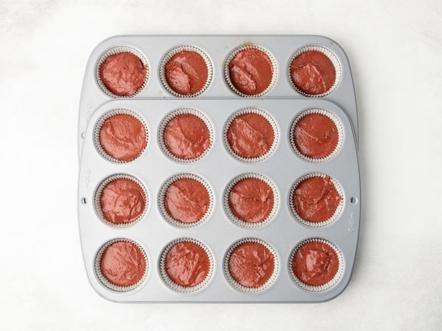 Raw reddish brown cupcake batter portioned into paper liners in a metal muffin tins layered on top of one another to make 16 cups of batter.