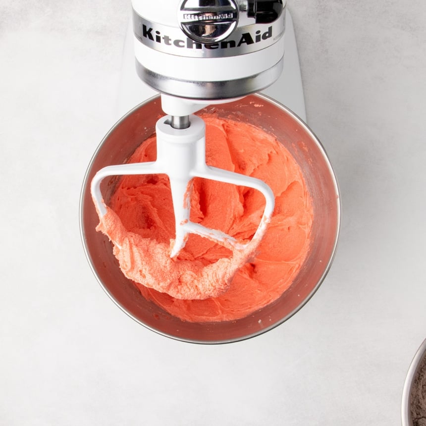Bright red batter mixed in a stand mixer bowl with a paddle attachment.