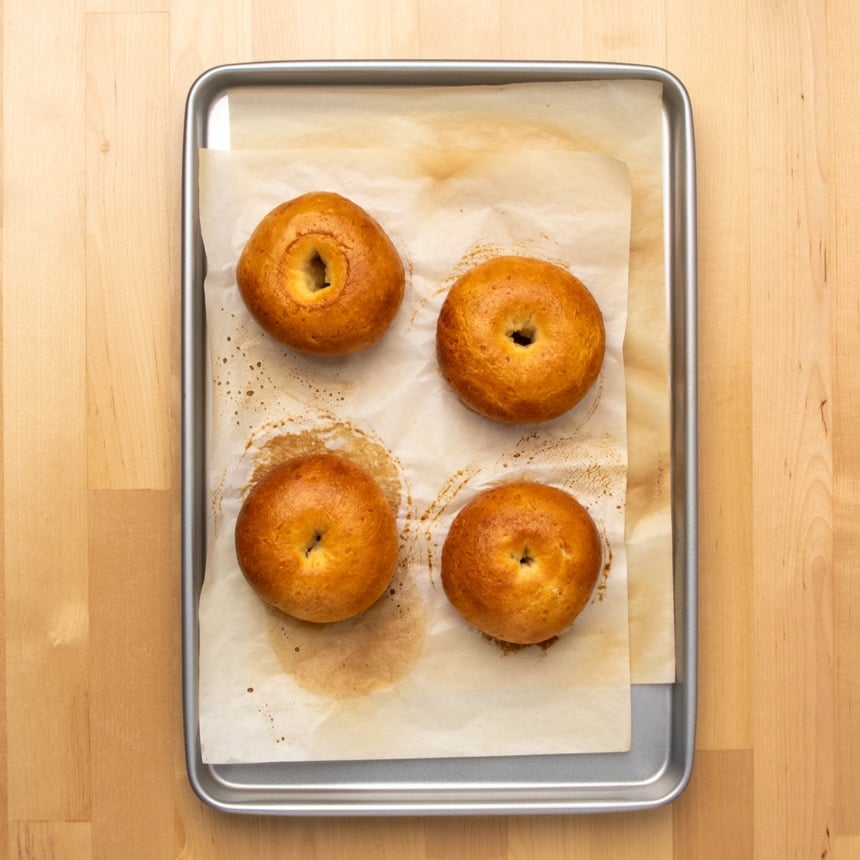 Four baked golden brown gluten free bagels on parchment paper in a baking sheet.