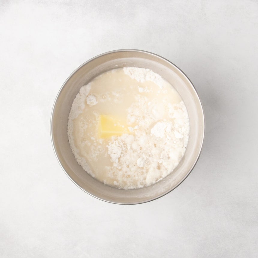Metal mixing bowl containing dry ingredients with unmixed additions of butter and liquids.