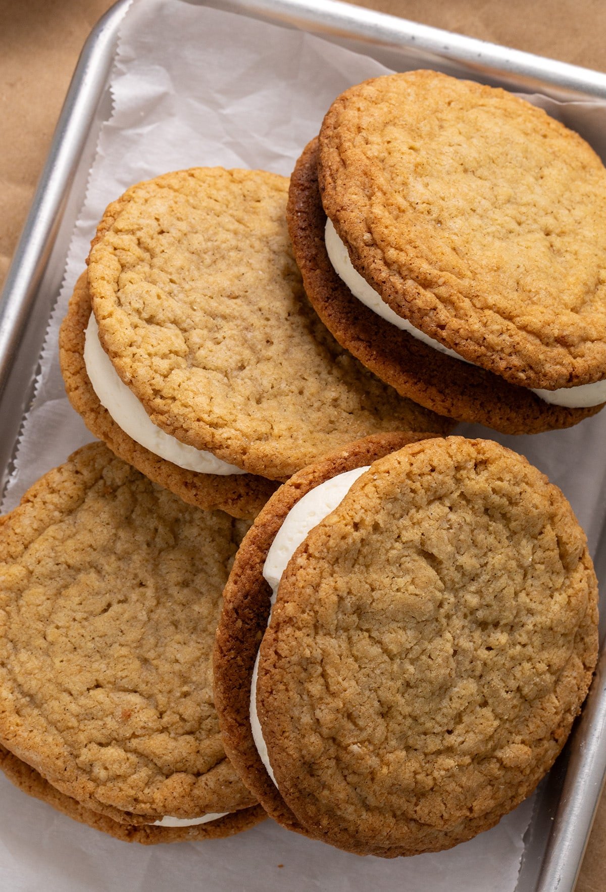 Overhead view of oatmeal cream pie sandwiches on a parchment-lined metal tray.