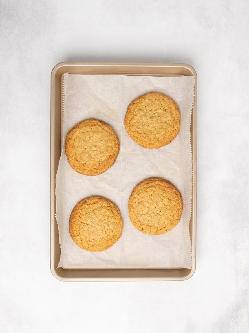 Overhead view of a parchment-lined baking sheet with four baked round cookies, golden brown and evenly spaced.
