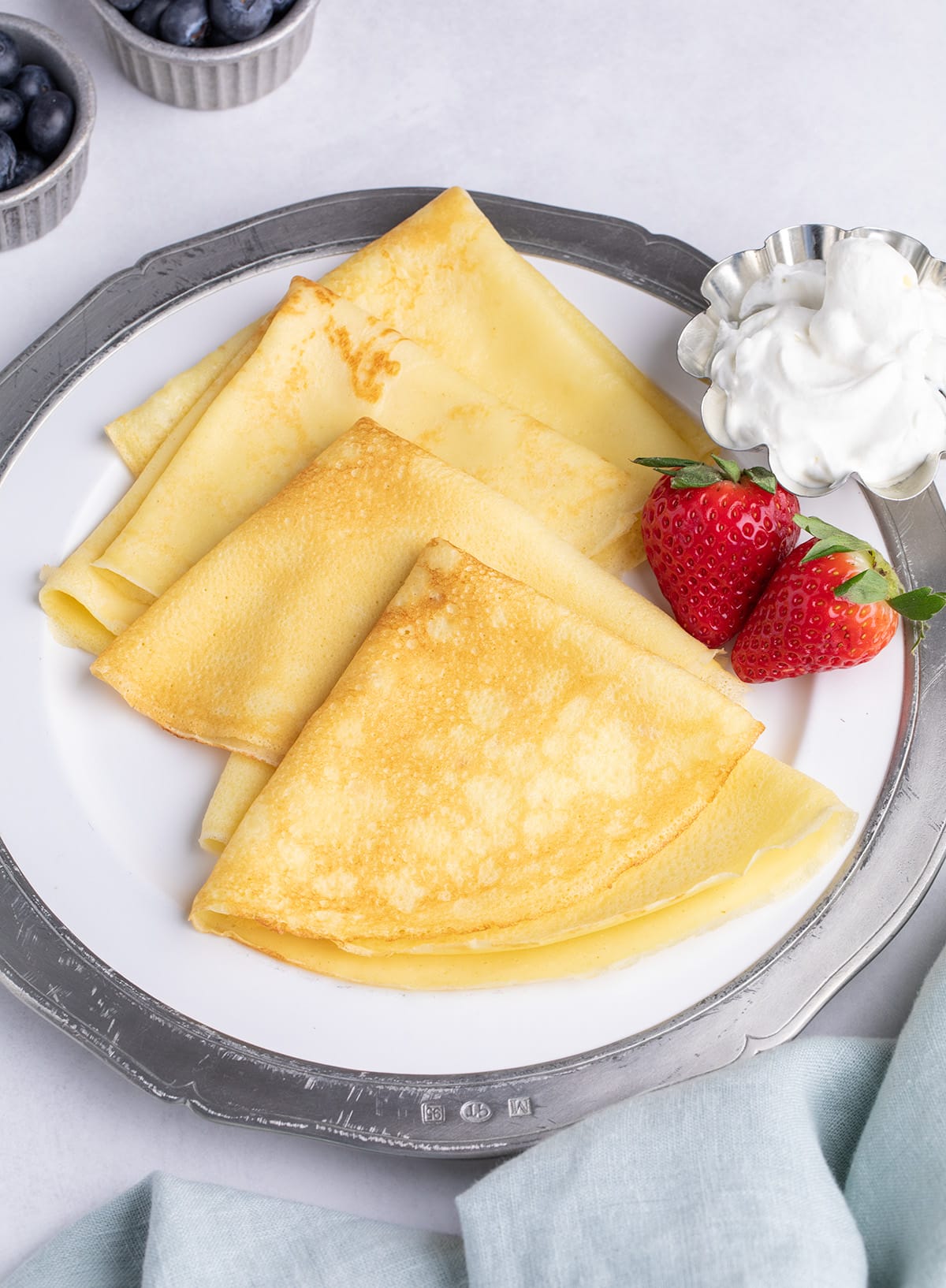 Closeup image of plate of 4 folded gluten free crepes with strawberries and a small dish of white cream.