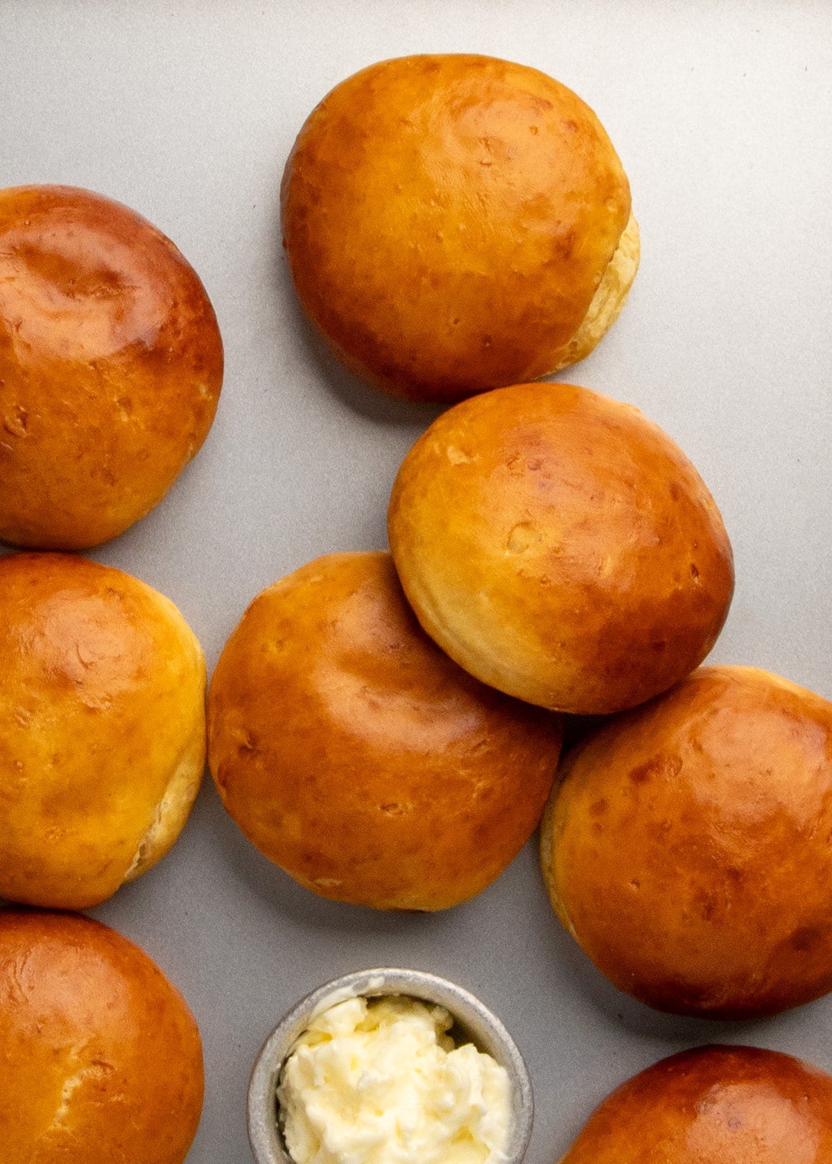 Portions of eight golden brown rolls arranged on a gray surface with a small dish of butter nearby.