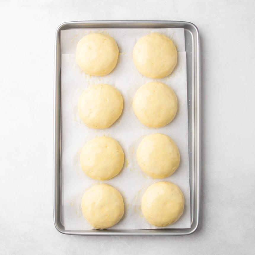 Smooth risen dough rounds arranged on a parchment-lined baking sheet.