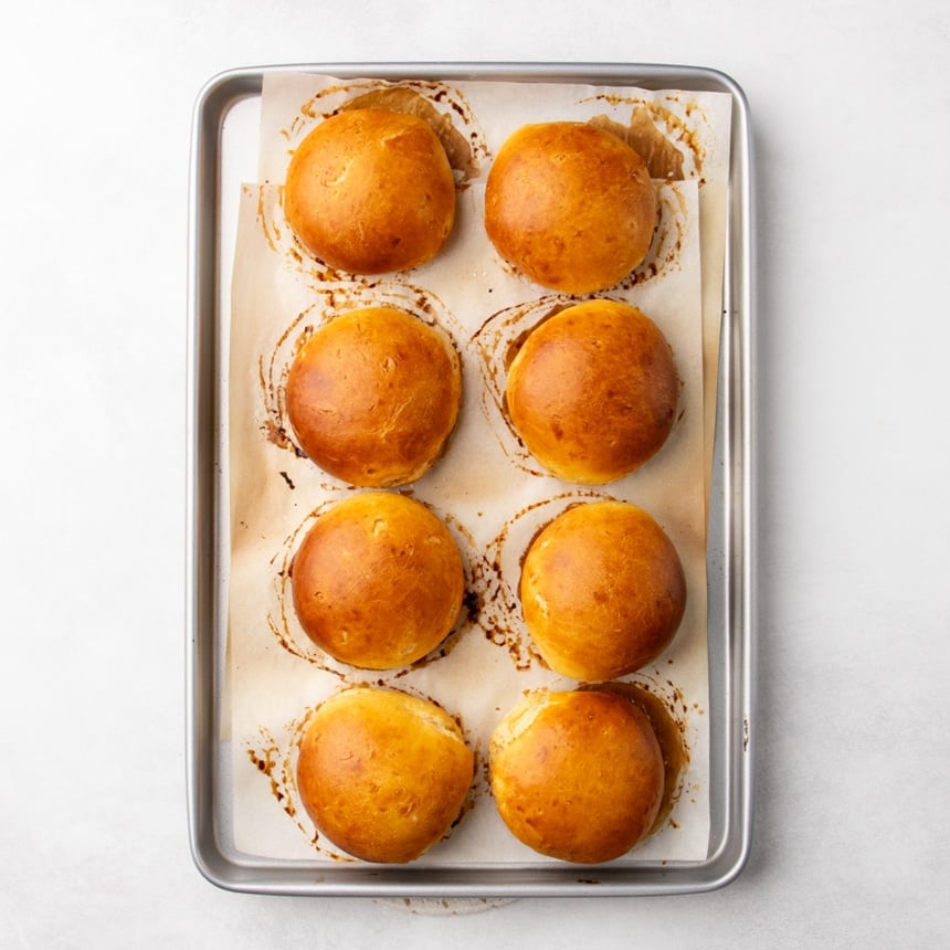 Baked golden brown rolls on a parchment-lined baking sheet with browned spots around each roll.