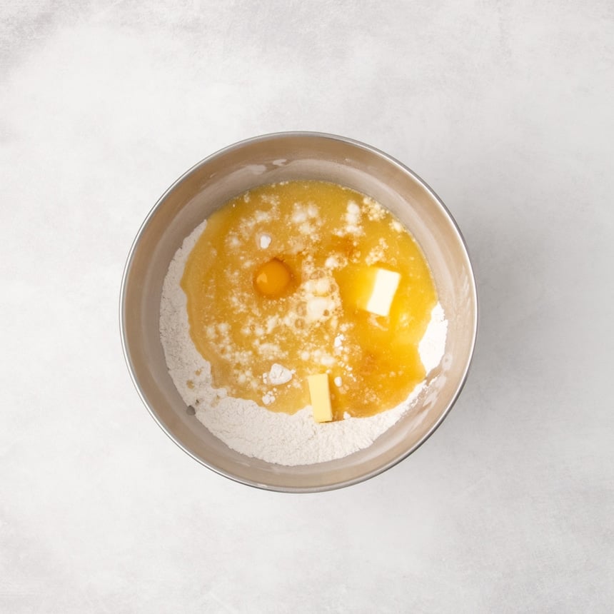 Wet ingredients sitting unmixed on top of dry ingredients in a mixing bowl with visible egg yolk and pieces of butter.